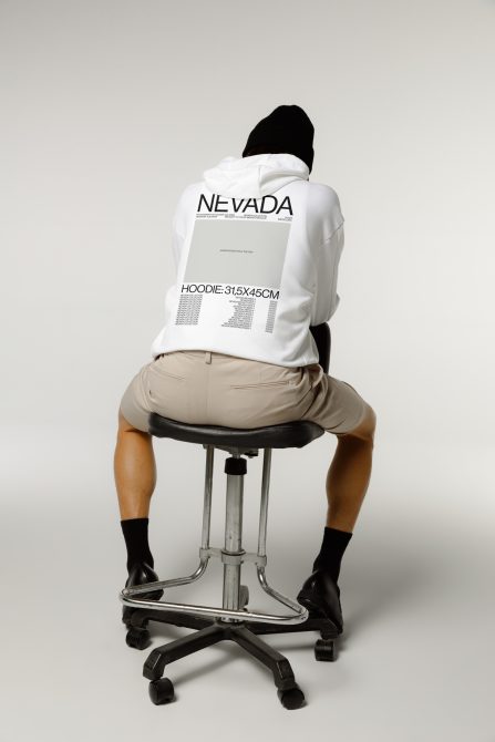 Rear view of person in white hoodie with print design, seated on stool, trendy mockup for fashion and apparel graphic display.