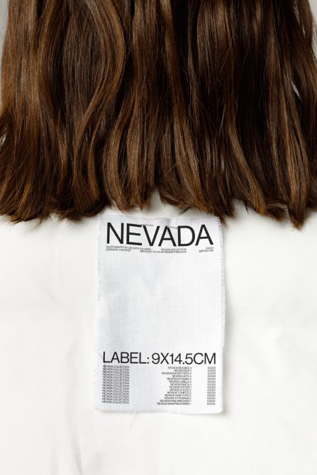 Brown wavy hair with white fabric label below showing Nevada branding, 9x14.5cm
