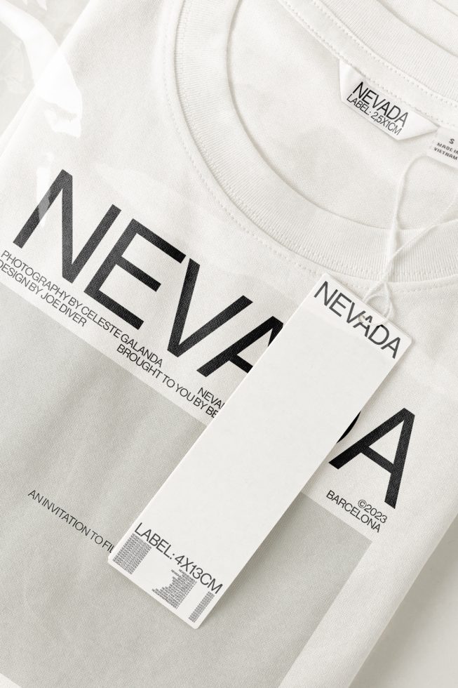 White T-shirt mockup with black NEVADA text design and hangtag, showcasing label branding, apparel design, and photorealistic texture.