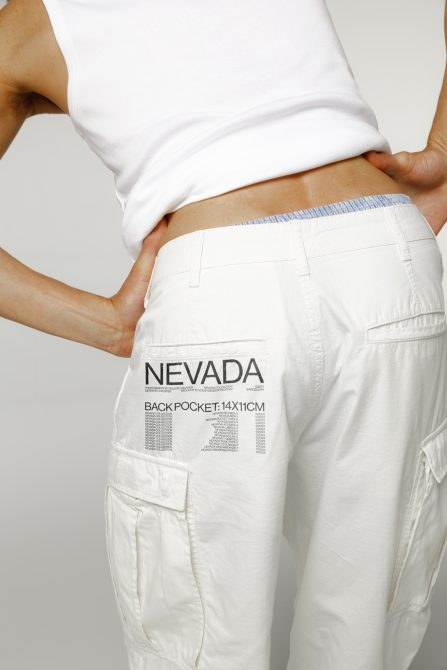 Close-up of white cargo pants mockup with text overlay design, showcasing back pocket size specifications for apparel design templates.