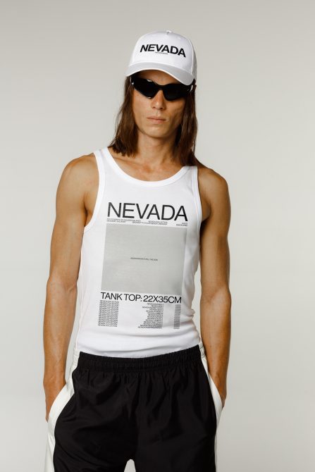 Male model in a white tank top and black shorts with NEVADA print, cap, and sunglasses for mockup graphics templates.