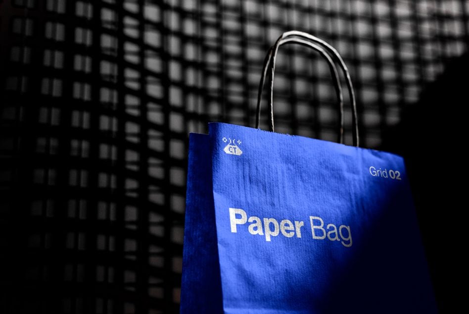 Bright blue paper bag with white text, rope handles, dark textured background