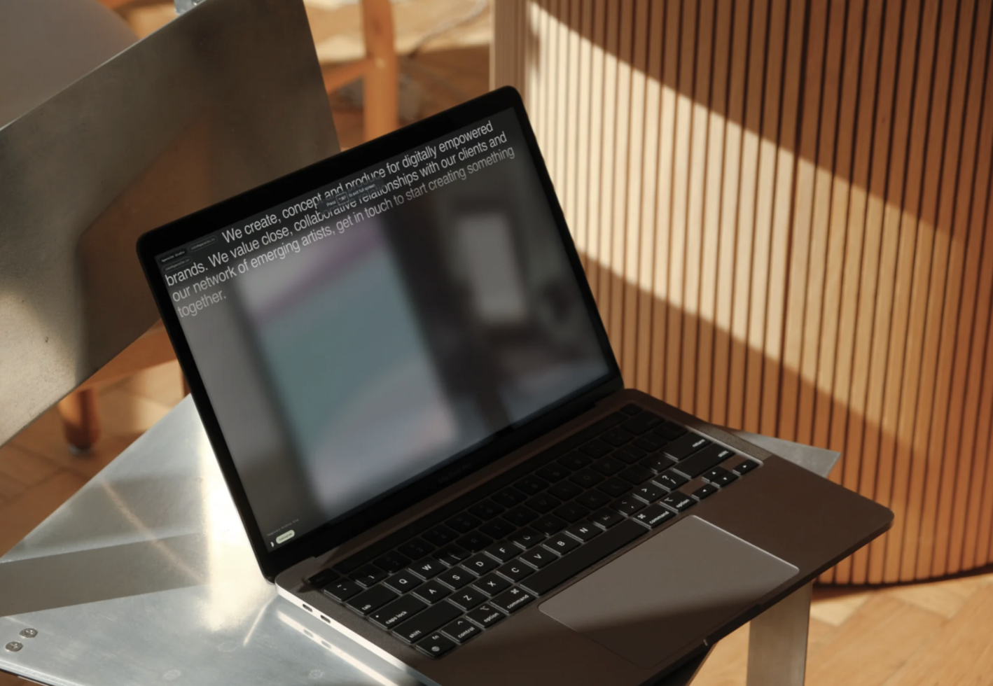 Laptop on metal table with text on screen in a sunny room, ideal for tech mockups, digital branding templates, or workspace graphics.