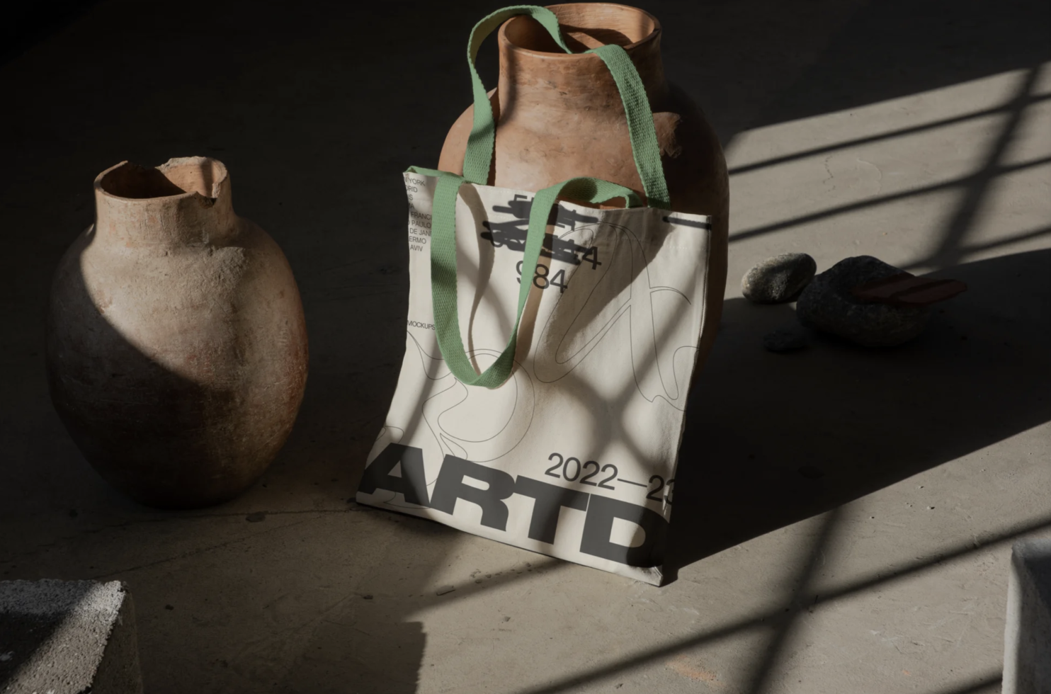 Artistic tote bag mockup with abstract design, sunlit shadows, and vintage pottery, perfect for designers' presentations.