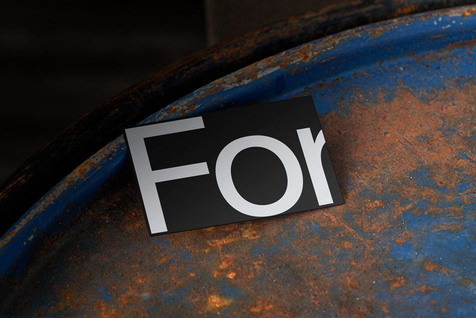 Business card with white FOR text on black background, tilted on rusty blue metal surface