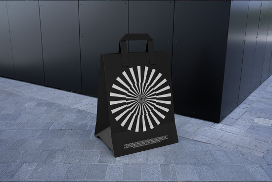 Black shopping bag mockup with geometric design standing on pavement, realistic display for presentation, outdoor branding.