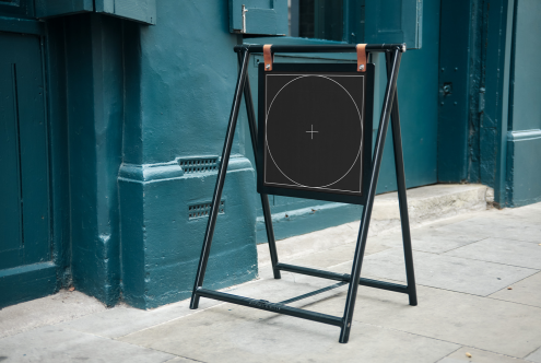 Sidewalk signboard mockup with a black frame and a blank canvas for design display, standing on a city street for graphic designers.