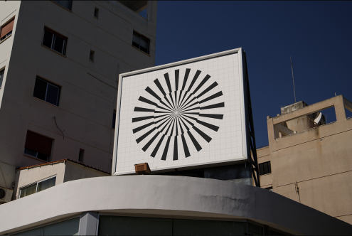 Graphic sunburst design billboard atop modern building, clear blue sky, urban setting, geometric lines, large format printing, design concept.