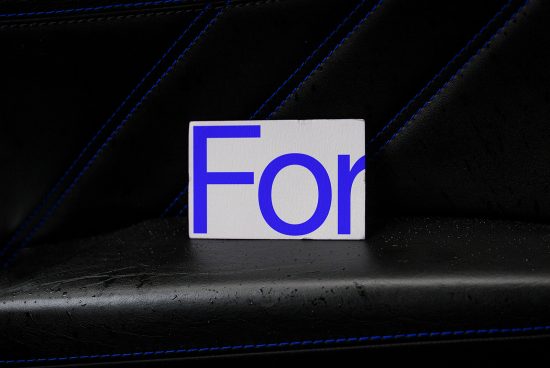 Blue and white typography card mockup on textured black seat with contrast stitching, perfect for font or logo display for graphic designers.