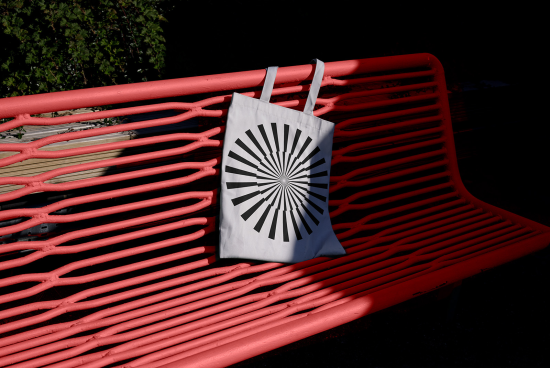 Canvas tote bag mockup with geometric pattern hanging on red park bench, showcasing product design concept, ideal for designers' presentations.