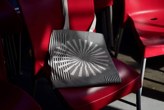 Stylish tote bag mockup with abstract pattern on a red chair, showcasing design and realistic shadows for product display.