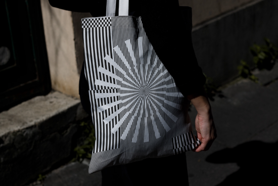 Black and white geometric patterned tote bag design mockup held by person, showcasing optical illusion, suitable for graphic design assets.