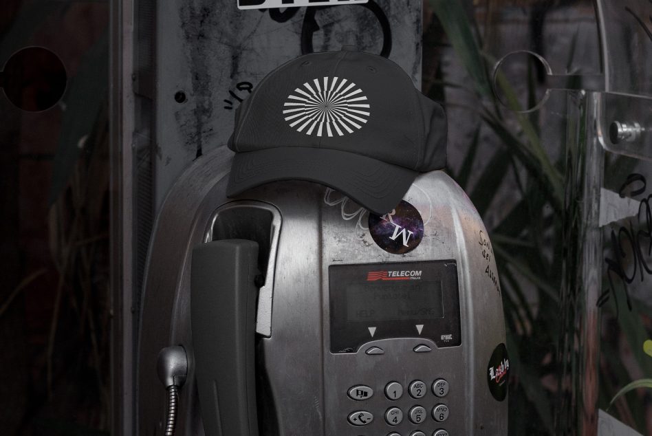 Distressed payphone topped with black cap featuring white starburst pattern