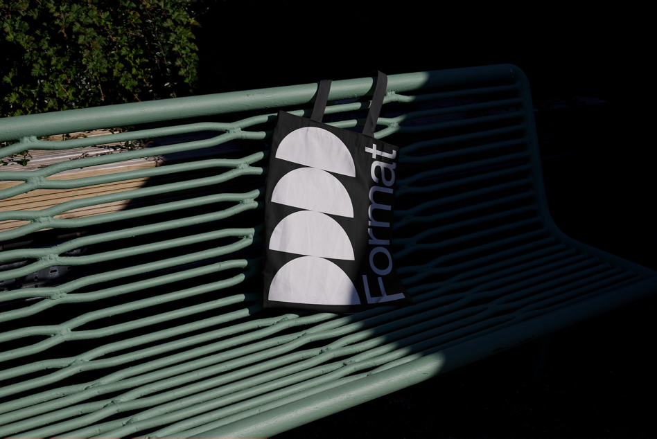 Black tote bag with white logo on green park bench, outdoor branding mockup for graphic designers, realistic shadows, natural light.