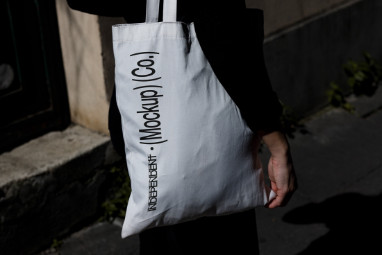 Person holding tote bag with 'Mockup[Co]' text, ideal for mockup graphics, branding, realistic template presentations, designer assets.