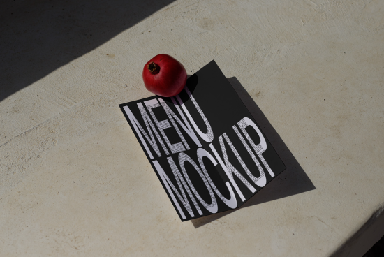 Realistic menu mockup design with a pomegranate weight on top placed on a concrete surface in sunlight, ideal for restaurant branding presentation.