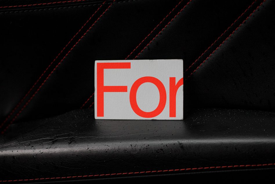 Bold red font typography "For" on white card against textured black leather with red stitching, ideal for mockup presentations.