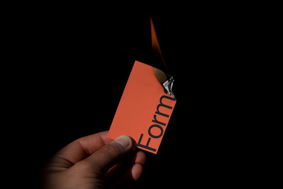 Hand holding a burnt orange card with the word Form partially visible, on a black background, showcasing bold typography design.