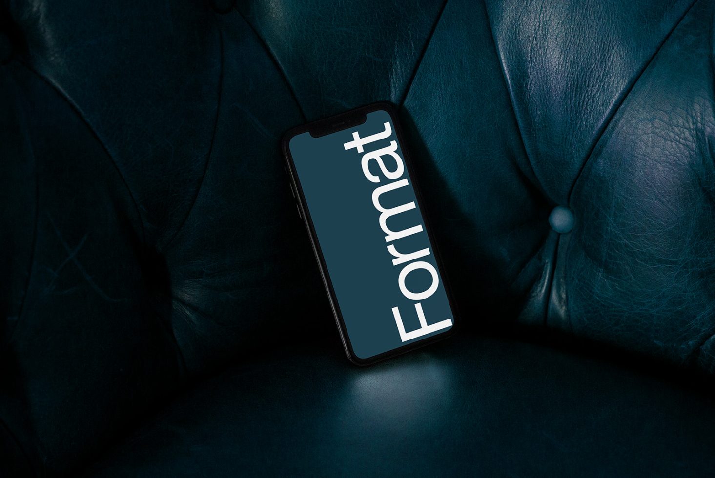 Smartphone on dark leather couch with screen showing word Format, ideal for mockup graphics in digital asset designs.