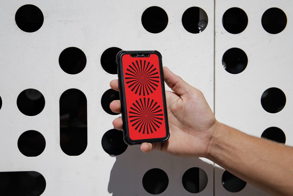 Hand holding smartphone with red and black geometric wallpaper, against dotted wall background, modern design element, graphic template mockup.