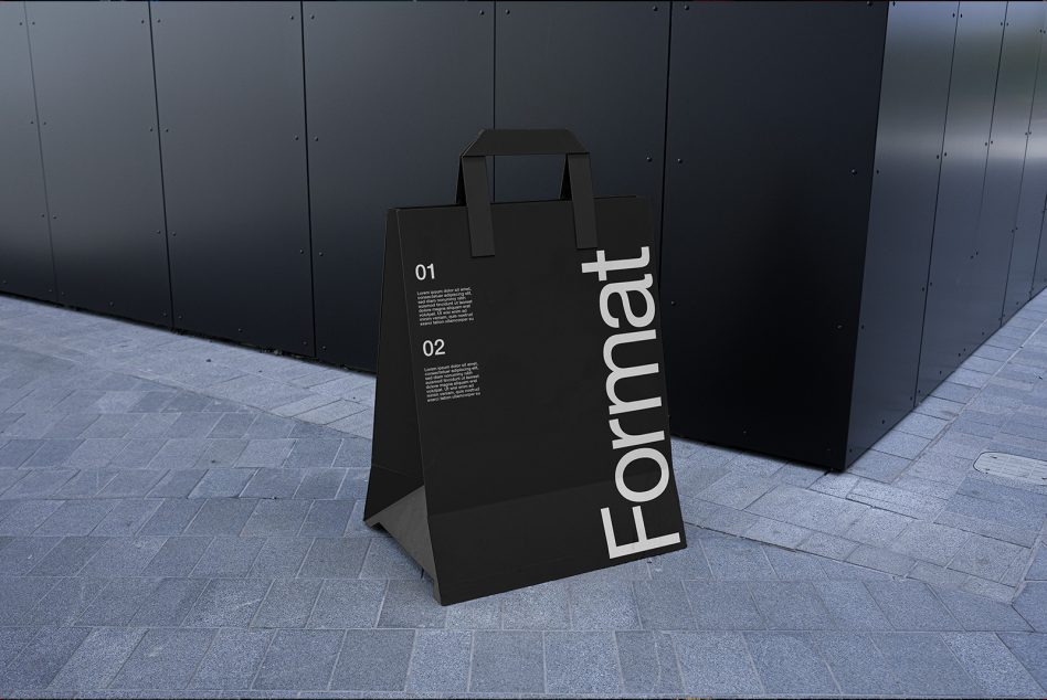 Black paper bag mockup with text graphics on city street background for designers, showcasing packaging design in urban setting.