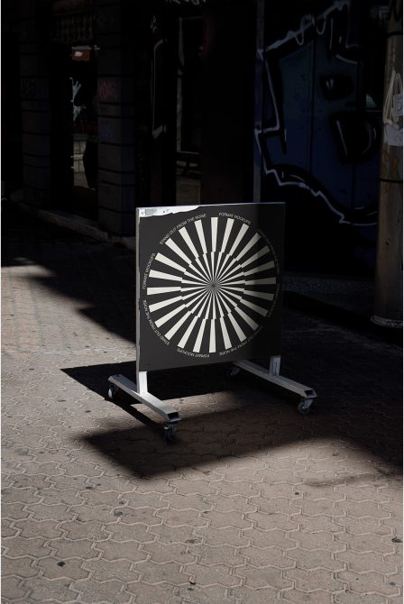Urban street mockup display on wheels with black and white op-art design for outdoor advertising, in a gritty setting with graffiti.