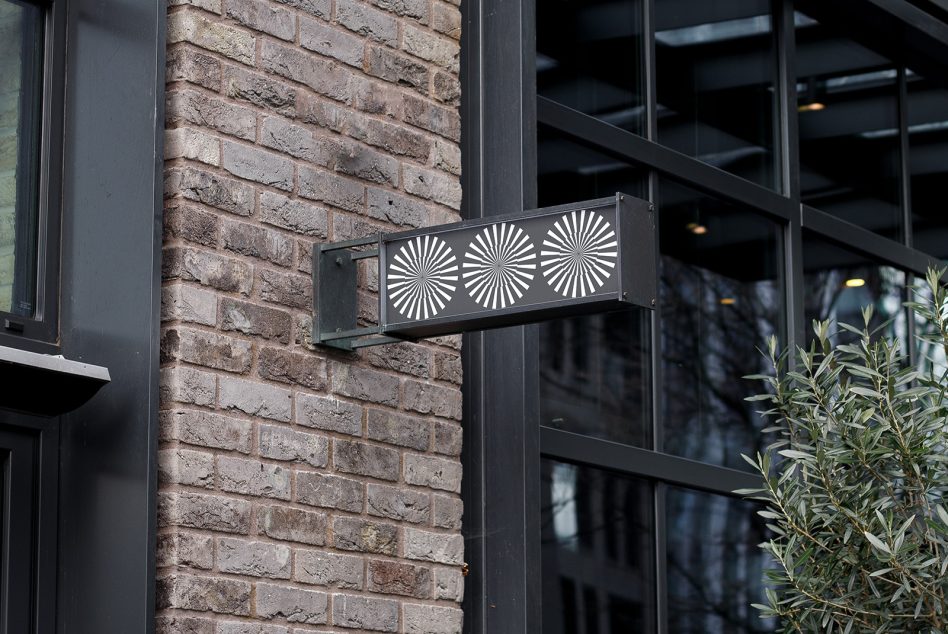 Outdoor hanging sign mockup on a brick wall by a store entrance, ideal for branding and logo design presentations.