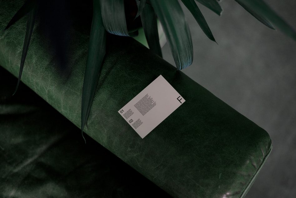 Elegant business card mockup on green velvet sofa with a tropical leaf, exuding premium design aesthetics for designers.