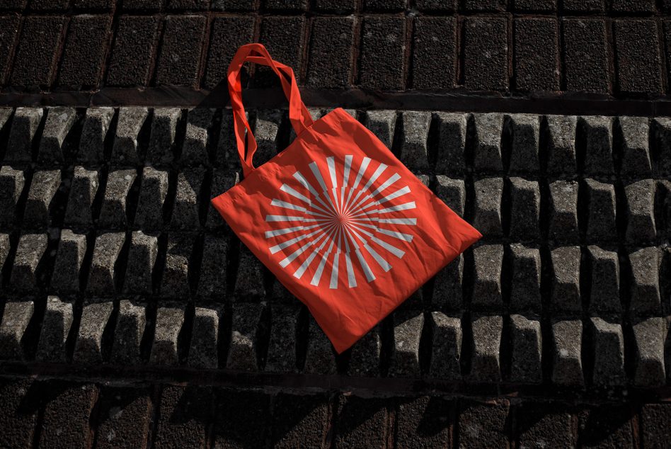 Red tote bag mockup with geometric design on cobblestone background in sunlight, ideal for showcasing patterns and branding.