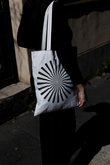 Woman carrying tote bag with black radial design, ideal for mockup template, showcasing contrast and urban style, perfect for designers' product display.