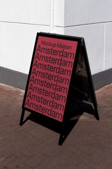 Black A-frame sandwich board with pink background, Amsterdam text stacked vertically