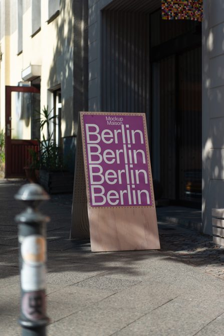 Light wood A-frame sign with purple Berlin lettering on sunlit urban street