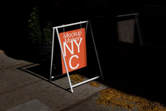 Street poster mockup on a sidewalk A-frame stand featuring "Mockup Maison NYC" design with dramatic lighting and autumn leaves.