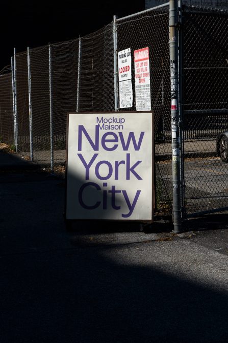 Cream colored square sign at chain-link fence with purple text saying New York City