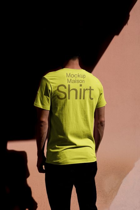 Rear view of a person wearing a bright yellow t-shirt mockup against a shadowed pink wall, ideal for fashion design presentation.