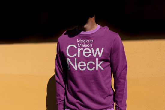 Purple crew neck sweatshirt mockup with person against orange wall, perfect for apparel design presentations.