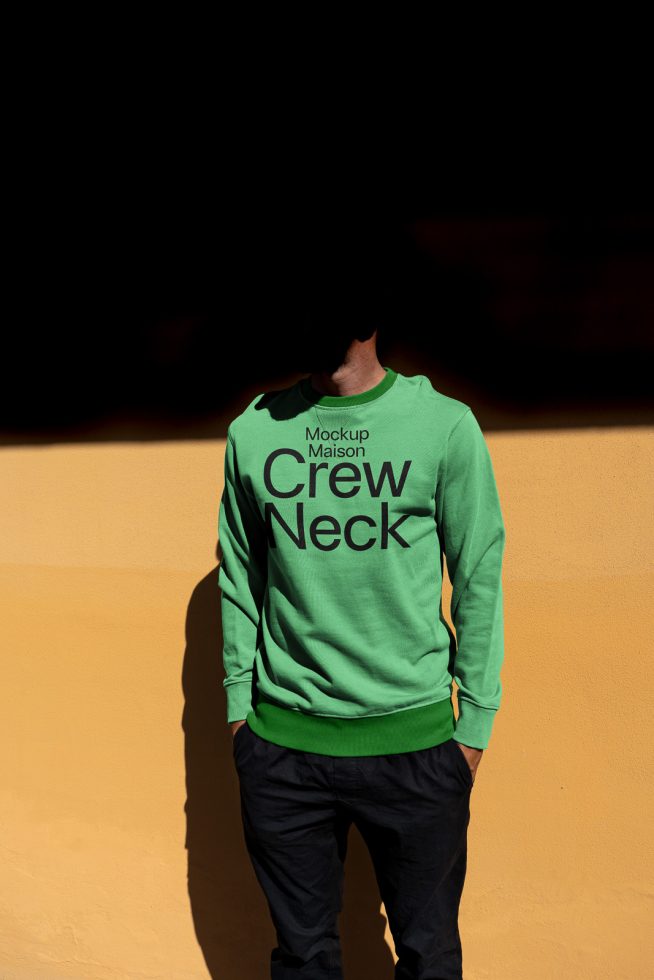 Person wearing green crew neck sweatshirt mockup against a yellow wall for fashion designers, ideal template for branding presentations.