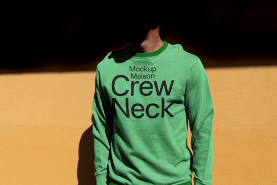 Person wearing a green crew neck sweatshirt mockup with shadow on orange wall, ideal for presentations and apparel design.