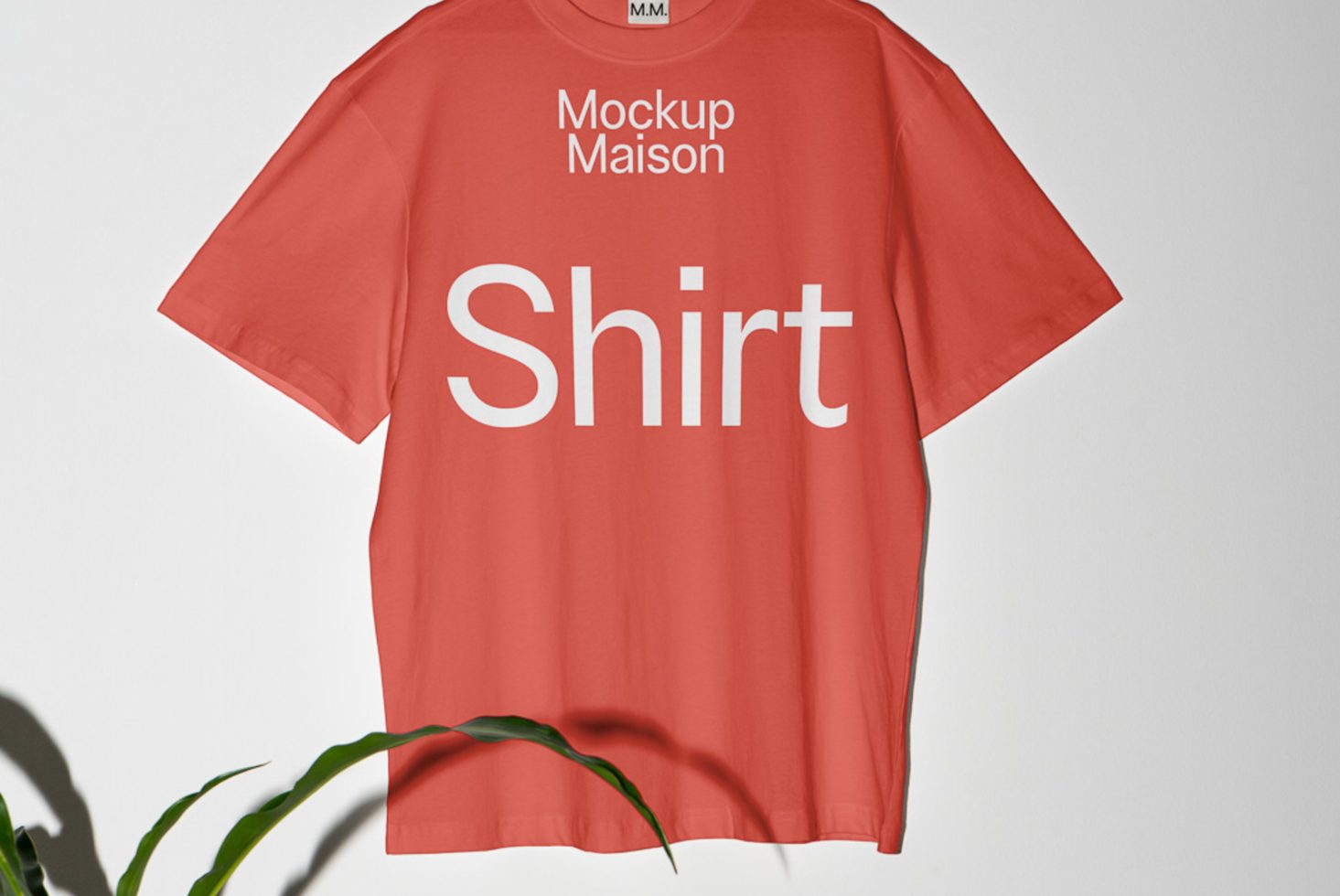 Alt: Red t-shirt mockup with white text design hanging against a plain background with plant shadow, ideal for apparel design presentations.