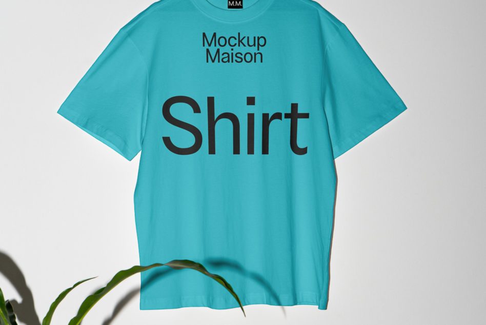 Turquoise oversized shirt on hanger with dark text, plant visible