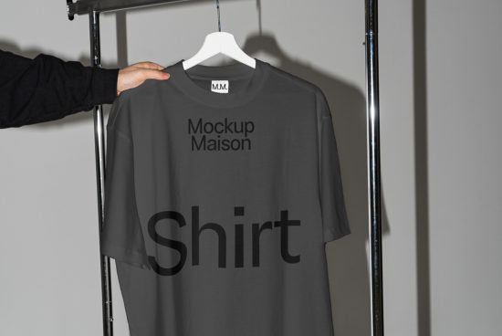 Person holding a T-shirt mockup on a hanger, with text for logo display, in a design studio setting, ideal for presentations and portfolios.