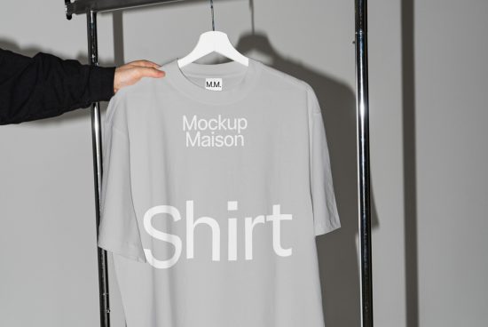 Person holding a plain gray t-shirt on a hanger for a mockup demonstration, clear for print design visualization, light studio setting.