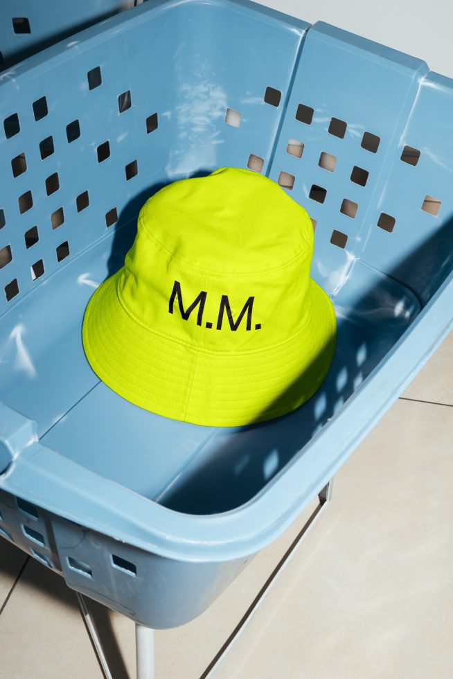 Bright yellow bucket hat with initials M.M. on blue plastic bin. Perfect mockup on tiled floor for fashion design showcase.