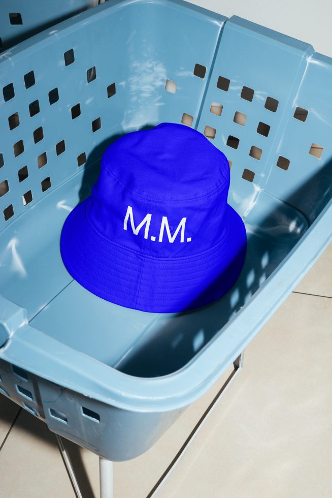 Blue bucket hat with white initials M.M. on a plastic crate, high-quality mockup for fashion accessory designs.