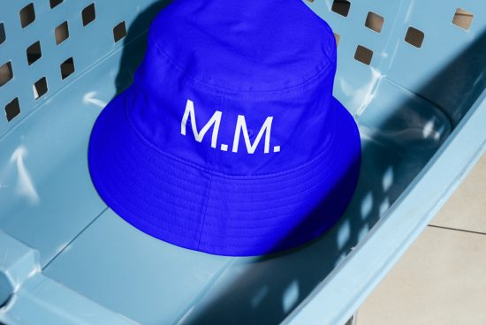 Blue bucket hat with white text resting in a plastic crate, ideal for fashion mockups, hat design previews, and branding visuals for designers.