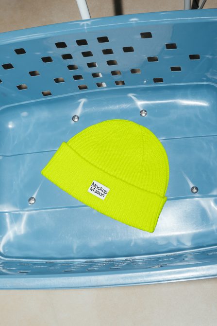 Bright neon yellow beanie hat mockup on blue chair, visible tag for logo placement, perfect for apparel design presentations.