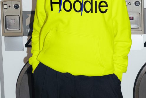 Person wearing vibrant yellow hoodie mockup with bold typography design in an urban laundry setting perfect for apparel presentations.