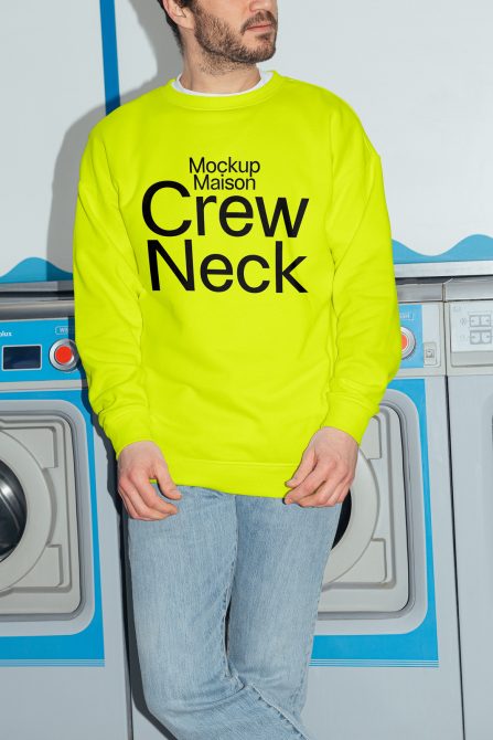 Man in neon yellow crew neck sweatshirt mockup, standing by washing machines, ideal for fashion design presentation.