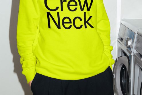 Bright yellow crew neck sweatshirt mockup on model in front of washing machines, trendy fashion apparel design display