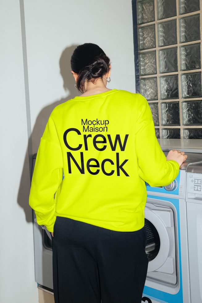 Woman in bright yellow crew neck sweatshirt mockup for design presentation, standing in a laundry room with washing machines.